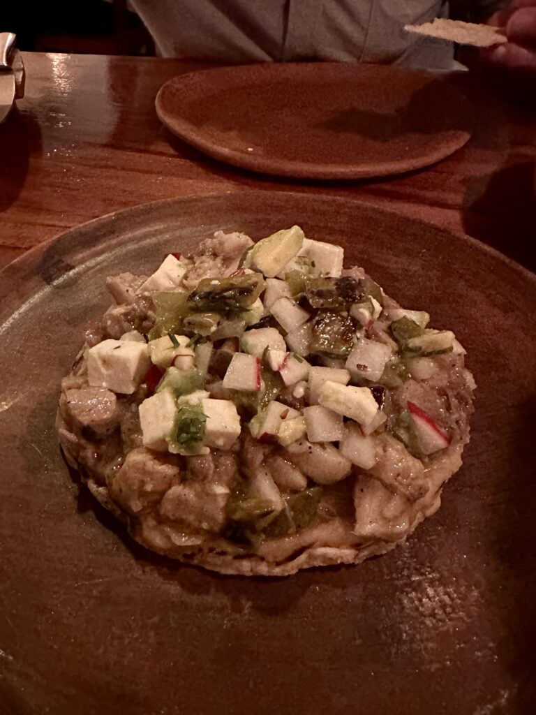 The standout dish of the night: succulent, slow-cooked pig's head at a Michelin-starred restaurant in Oaxaca, served with bold flavors in a breathtaking open courtyard setting.