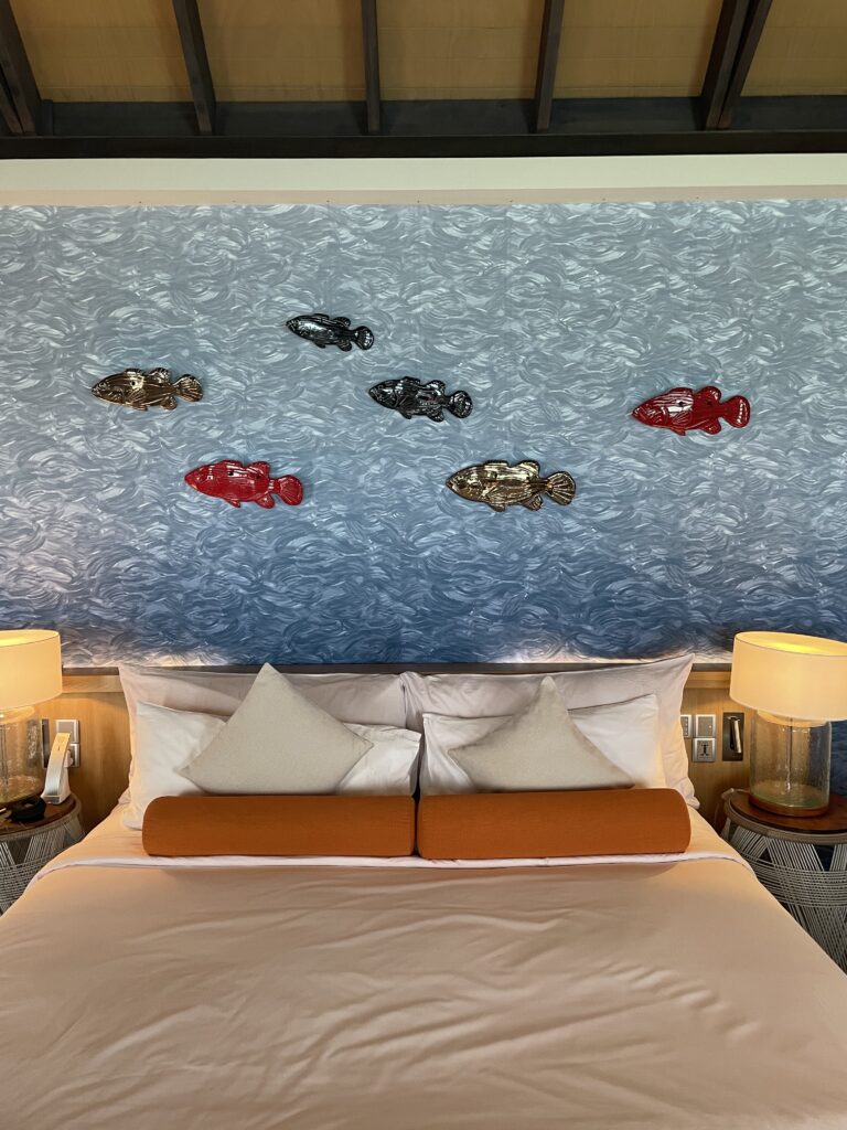 Experience ultimate comfort in the Wind Villa at Ozen Life Maadhoo with a king-sized bed featuring an aquatic-themed headboard, blending luxury and design.