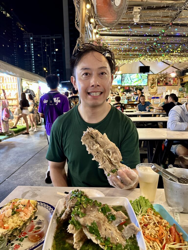 Holding up a massive Volcano Rib at Jodd Fairs night market in Bangkok, showcasing the rib's size and spicy glaze.