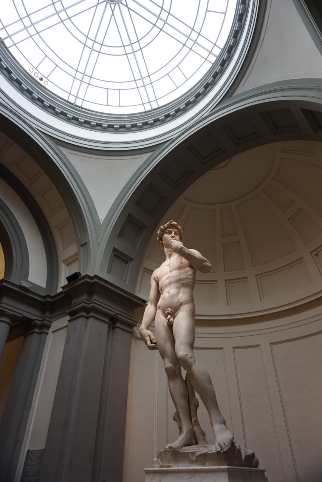 Full-body image of Michelangelo’s David standing under the skylight in the Accademia Gallery