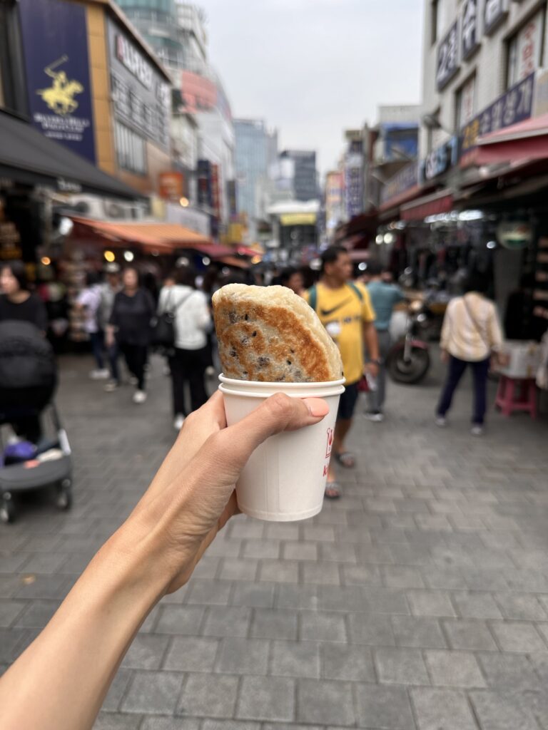 Hands holding a golden, crispy hotteok from Namdaemun Market.