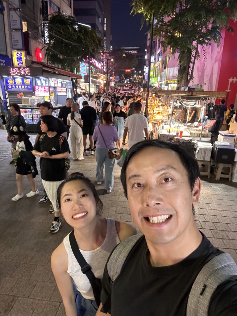 People enjoying Korean street food like fish cakes and dumplings at the popular Myeongdong Night Market in Seoul