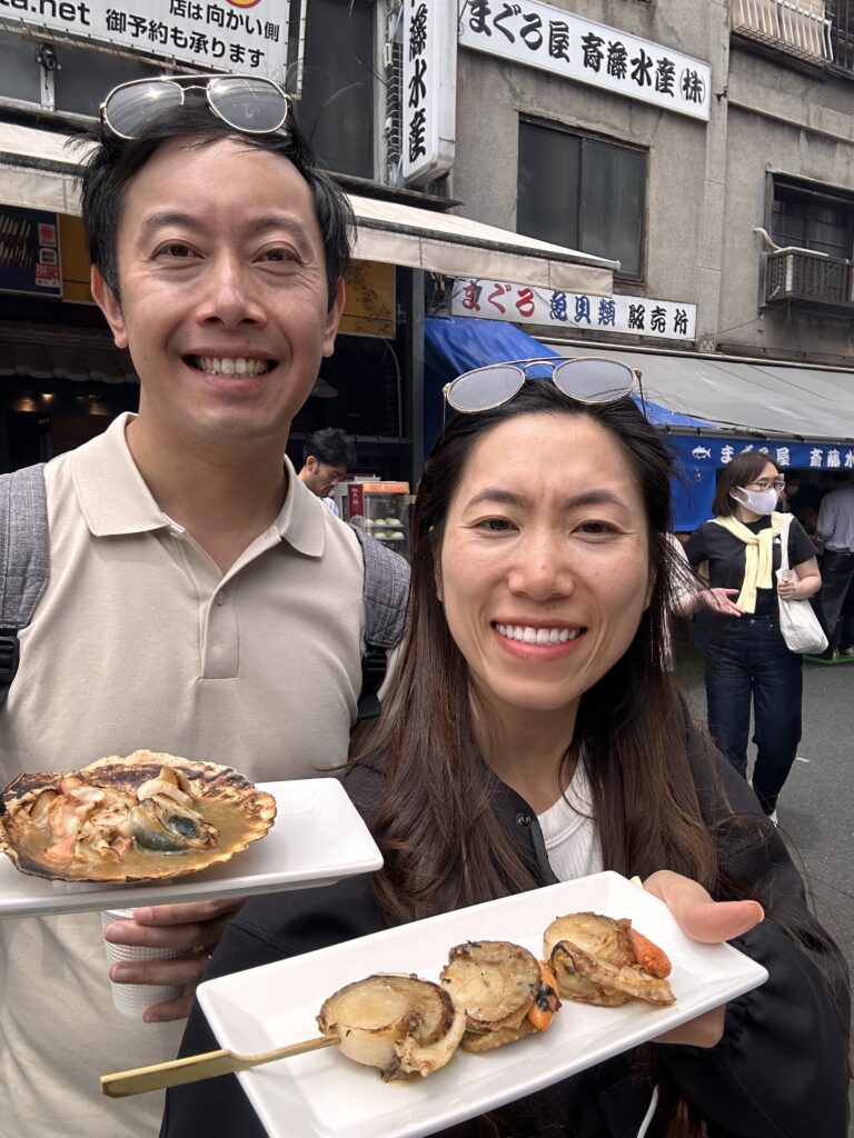 Couple enjoying fresh scallops grilled in front of them at Tsukiji Market Tokyo