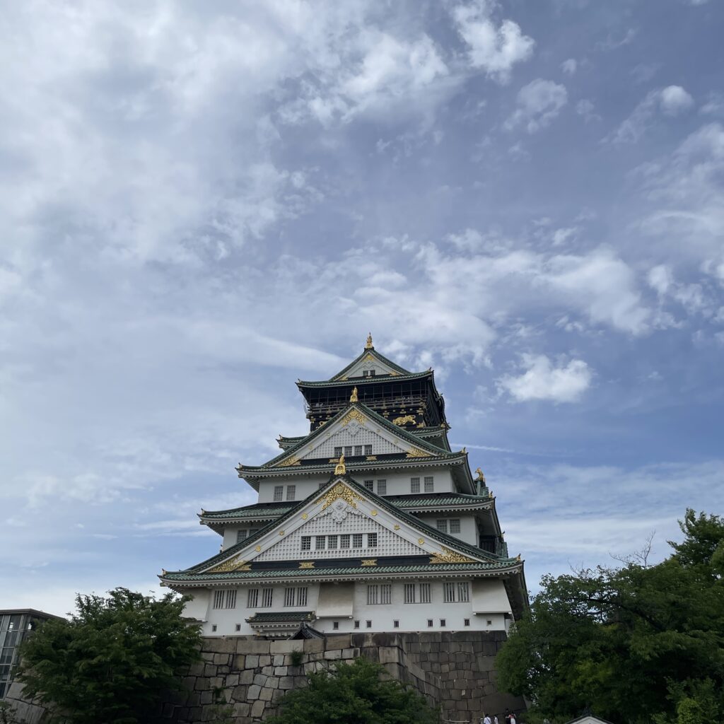 Osaka Castle rising above the surrounding park, with people exploring its historic grounds.