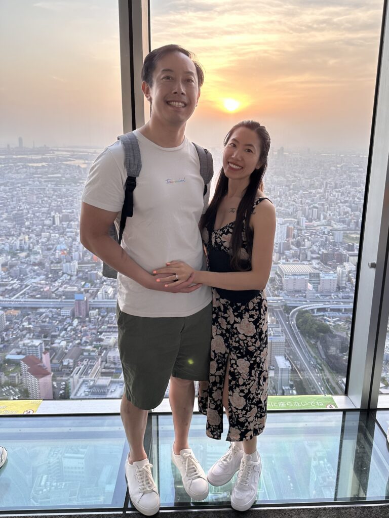High above Osaka, the sunset from Abeno Harukas reveals a layered horizon — deep orange sky, dark mountains, glittering bay, and the sprawling city below.