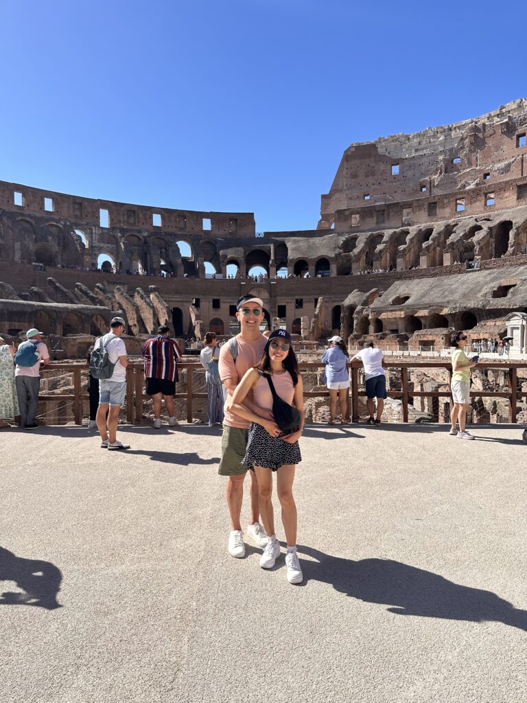 Interior of the Colosseum showing the vast oval arena, underground chambers exposed to view, and tiered seating rising high, filled with the atmosphere of history and the buzz of modern visitors